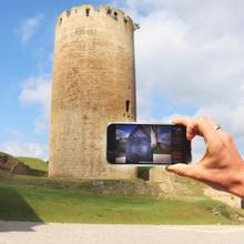 Im Vordergrund hält eine Hand ein Smartphone mit einem Bild. Dahinter der Turm Dicker Wilhelm. Blauer Himmel ©Set Jetting UG
